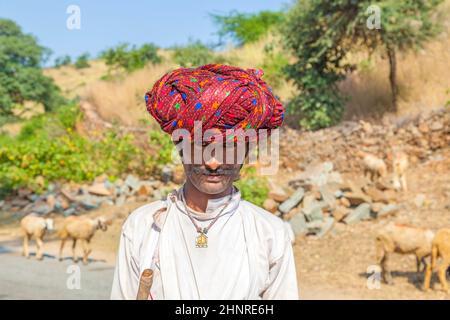 Un uomo tribale del Rajasthani che indossa il turban rosso colorato tradizionale e protegge le capre Foto Stock