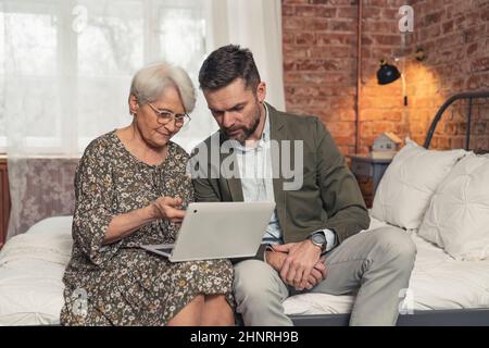 moderna madre in pensione nel suo 70s mostrando al figlio di mezza età qualcosa sul suo laptop. Foto di alta qualità Foto Stock