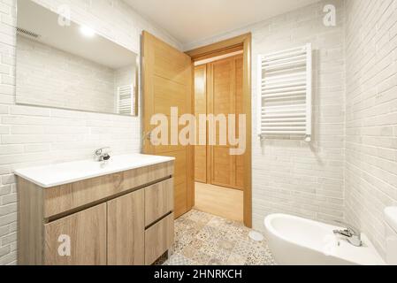 Bagno in mattoni bianchi a vista con lavandino in legno, porte in legno, pavimento in piastrelle di cemento e lavandino in porcellana bianca Foto Stock