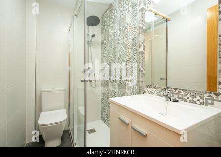 Bagno con pareti piastrellate lisce e motivi idraulici con specchio quadrato senza cornice e lavabo bianco Foto Stock