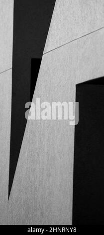 disegno astratto di ombre sulla parete esterna grigia bianca dell'edificio che crea forme geometriche in bianco e nero angoli e linee sfondo verticale Foto Stock