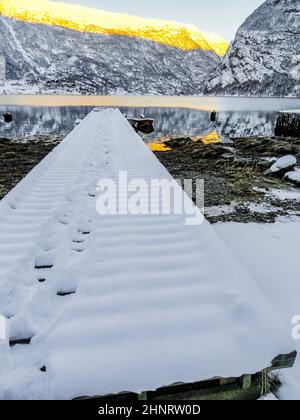 Molo innevato in un paesaggio invernale presso il lago dei fiordi di Framfjorden, Vestland, Vik, Norvegia. Foto Stock