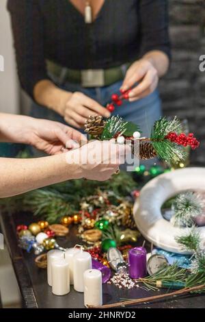 Due donne stanno preparando la corona di avvento e le decorazioni di Natale. In verticale. Foto Stock