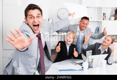 Un uomo d'affari entusiasta con un team felice che celebra la vittoria Foto Stock