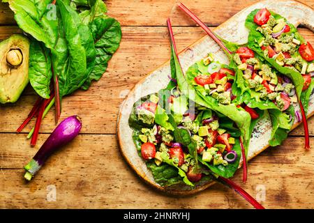 Insalata di vitamina estiva su tavola da cucina. Insalata di avocado, pomodoro con salsa all'aglio in foglie di bietole. Foto Stock