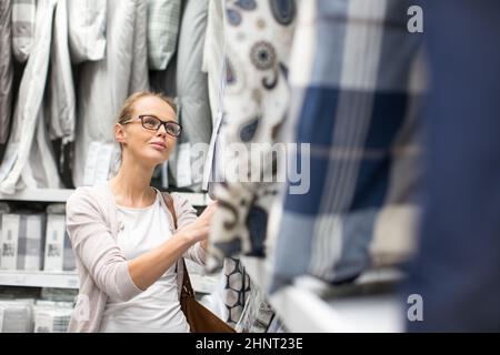 Piuttosto, giovane donna scegliere il diritto di fogli per il suo letto in un moderno arredamento home store (colore immagine dai toni shallow DOF) Foto Stock