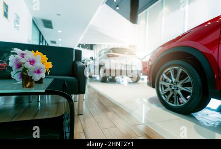 Area ricevimento clienti e lussuosa auto SUV color rosso e bianco sfocato parcheggiata in un moderno showroom. Concessionario di auto e leasing auto concetto. Industria automobilistica. Interno dello showroom. Nuovo stock di auto SUV in vendita. Foto Stock