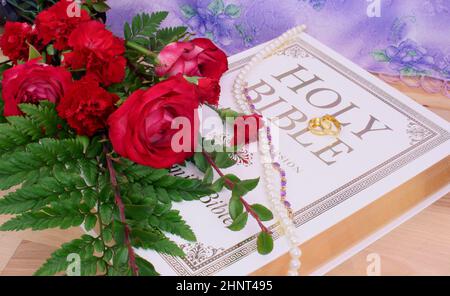 Rose e anelli di nozze e gioielli sulla Sacra Bibbia Foto Stock