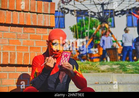 Street performer che mette sul suo make-up viso. Gli artisti di strada possono ingannare i passanti e intrattenere i turisti. Foto Stock