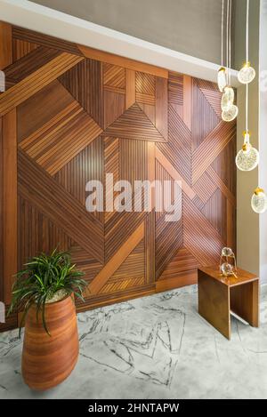 Pareti rivestite in legno, moderno lampadario alto in vetro, alto piantatore con cespugli e pavimento in marmo bianco Foto Stock