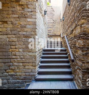 Muro in mattoni di pietra con una stretta scala in legno vecchio tempo che sale con corrimano in legno, in edificio abbandonato Foto Stock