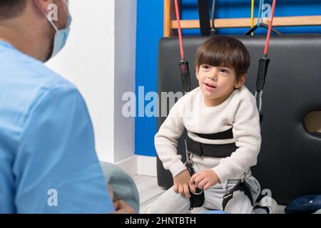 Cute capretto con paralisi cerebrale che fa la terapia muscoloscheletrica in ospedale mentre ride e si diverte. Foto Stock