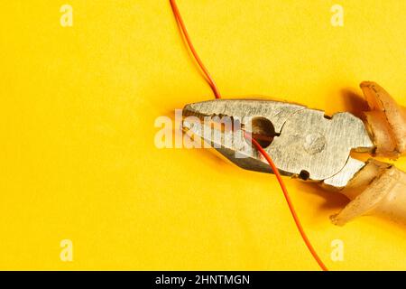 La pinza taglia un filo rosso su sfondo giallo. Attrezzatura. Copiare spazio Foto Stock