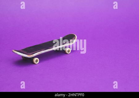 Skateboard piccolo su sfondo viola. Skate piccolo per le dita. Primo piano con la tastiera. Spazio per la copia Foto Stock