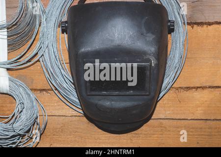 Maschera protettiva per saldatura appesa su una parete di legno. Cannelli di corda di acciaio. Casco per fermano Foto Stock