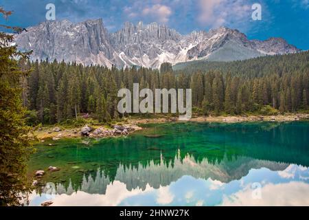 Panorama del Lago di Carezza un lago alpino circondato da un'alta pineta nelle Dolomiti con vista sulla catena montuosa del Rosengarten sullo sfondo in South Tyr Foto Stock