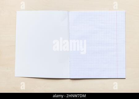 vista dall'alto della prima pagina vuota del quaderno aperto con fogli quadrati con margini su asse di legno marrone chiaro Foto Stock