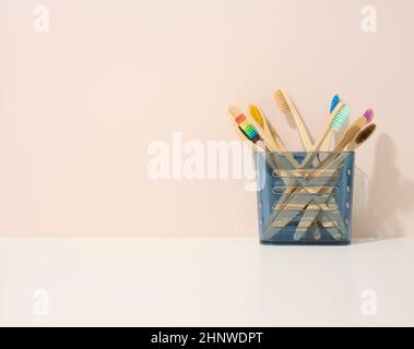 spazzolini in legno in una tazza di plastica su un tavolo bianco. Sfondo beige, zero sprechi. Spazio di copia Foto Stock