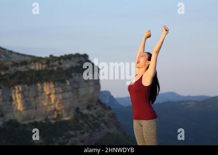 Felice runner sollevare le armi celebrare in una scogliera di montagna Foto Stock