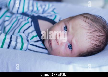 Un ragazzino in un vestito a righe sul serio e schienate guarda nella fotocamera, sdraiato su un cuscino bianco. Foto di alta qualità Foto Stock