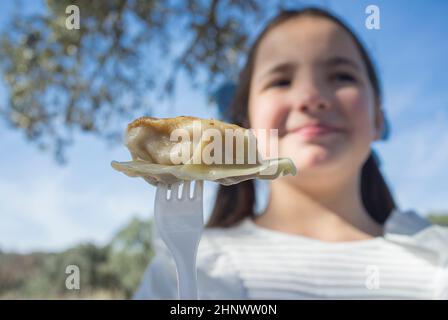 Bambina con jiaozi pezzo su forchetta. Sfondo esterno Foto Stock