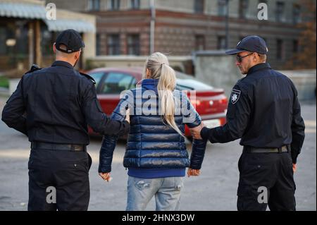 Due poliziotti maschi arrestano la giovane donna. I poliziotti in uniforme proteggono la legge, la registrazione di un reato. Poliziotti lavorano su strade, ordini e jus della città Foto Stock