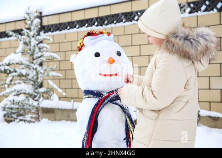 La ragazza fa un pupazzo di neve. Un bambino dipinge un sorriso ad un pupazzo di neve. Una partita nella stagione invernale. Foto Stock