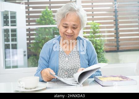 Donna anziana o anziana asiatica che legge un libro per il cervello di pratica mentre vive a casa, concetto di pensionamento hobby di riposo. Foto Stock