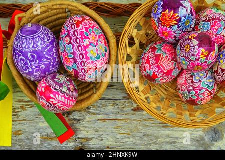 Vita morta con uova di Pasqua. Le uova di Pasqua decorate si trovano in un cestino di vimini su uno sfondo di legno bianco, vista dall'alto. Uova di Pasqua, decorate con tradizione Foto Stock