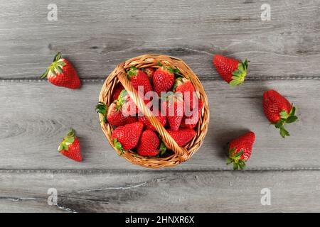 Tabella top view - cesto di fragole, alcuni versato sul grigio scrivania in legno. Foto Stock