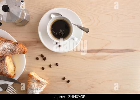 Tazza bianca in porcellana con caffè caldo, croissant e fagioli su tavola di legno marrone a colazione. Vista dall'alto. Composizione orizzontale. Foto Stock