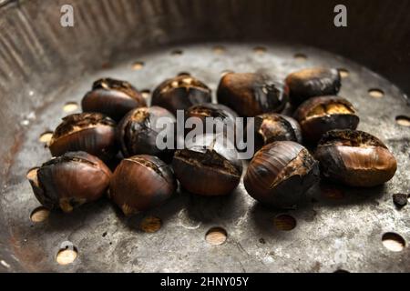 castagne arrosto nella tipica padella forata Foto Stock