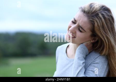 Ragazza adolescente che soffre di mal di collo all'aperto in un campo Foto Stock