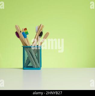 spazzolini in legno in una tazza di plastica su un tavolo bianco. Sfondo verde, zero sprechi. Spazio di copia Foto Stock