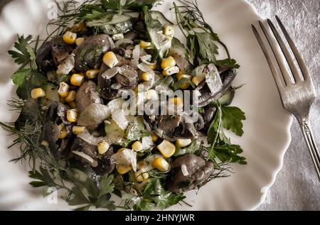 Sul tavolo di un piatto c'è un'appetitosa insalata di funghi, cipolle, mais in scatola e cetrioli. Vista dall'alto, primo piano Foto Stock