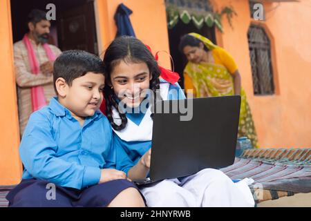 Felice ragazzo indiano giovane e ragazza usando il portatile. Fratello e sorelle o amici che indossa uniforme scuola tenendo computer, l'istruzione online e la scuola domestica Foto Stock