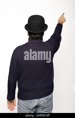 L'uomo girato da dietro indica con il dito un punto verso l'alto. Indossa un maglione blu, jeans e un cappello da bowler. Isolato su sfondo bianco Foto Stock