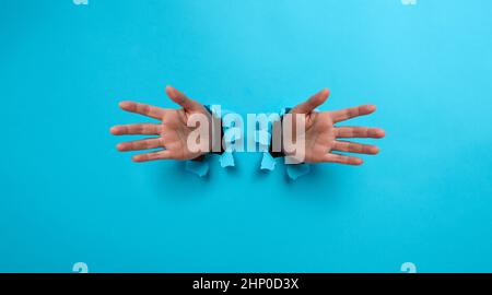 due palme femminili che sporgono da un foro strappato in carta blu Foto Stock