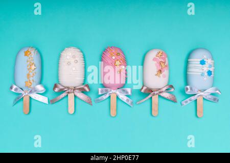 La torta decorata pops gelati con archi in fila su sfondo turchese. Vista dall'alto. Foto Stock