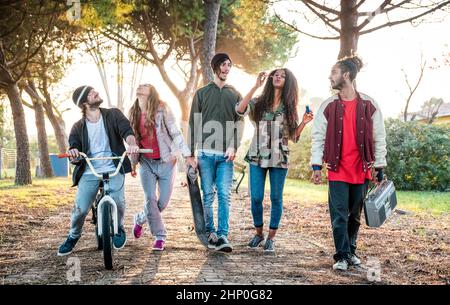 Amici urbani gang camminare in città skatepark al tramonto controluce - concetto di amicizia giovanile e millenaria con i giovani multirazziale che si divertono tog Foto Stock