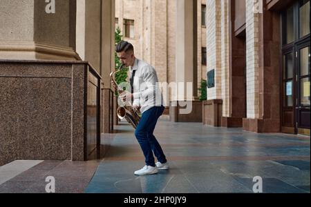 Il sassofonista maschile suona il sassofono per strada, giovane talento. Musicista con sax all'aperto, performance musicale in città, jazz performer Foto Stock
