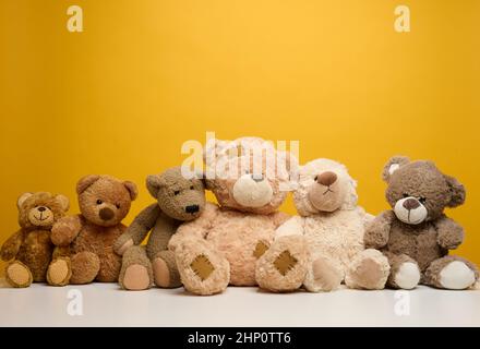 gruppo di graziosi orsacchiotti marroni si siedono su sfondo giallo, giocattolo per bambini Foto Stock