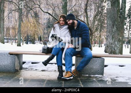 coppia a piedi in città. Giovane uomo d'affari in giacca blu con barba. E una donna carina in cappotto lungo. Vacanza in famiglia e convivenza, data Foto Stock