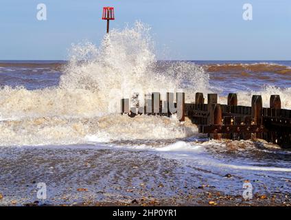 Onde che si infrangono sulle difese del mare di legno a Walcott, Norfolk durante i mari accidentati a seguito di una tempesta che provoca spruzzi e schiuma di mare. Foto Stock