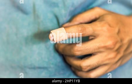 Primo piano di un bendaggio su un dito indice di un uomo su sfondo blu. Assistenza sanitaria pronto soccorso emergenza recupero. Foto Stock