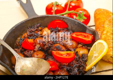 Baby seppie arrostite in padella di ferro con pomodori e cipolle su tavola in legno rustico Foto Stock