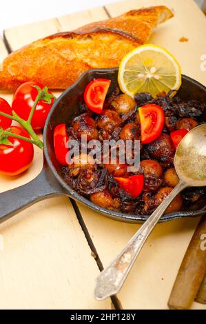 Baby seppie arrostite in padella di ferro con pomodori e cipolle su tavola in legno rustico Foto Stock