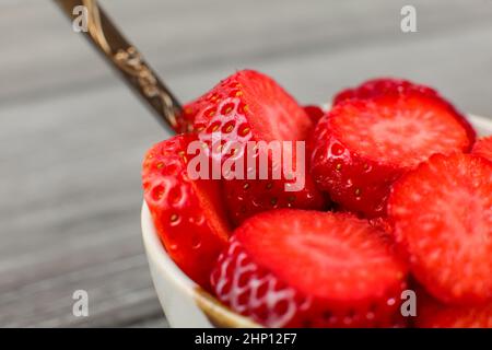 Close up - piccola ciotola con cucchiaio pieno di fragole tagliate a piccoli pezzi di cerchio. Pronto a mangiare snack sani. Foto Stock
