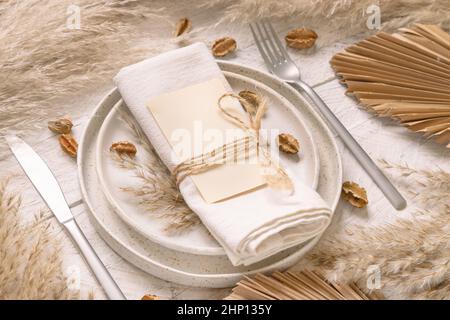 Tavolo posto con carta bianca su tavolo di legno bianco con decorazioni bohémien intorno primo piano. Boho menu di nozze carta mockup. Modello beige tropicale wi Foto Stock