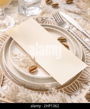 Tavolo posto con carta bianca su tavolo di legno bianco con decorazioni bohémien intorno primo piano. Boho menu di nozze carta mockup. Modello beige tropicale wi Foto Stock